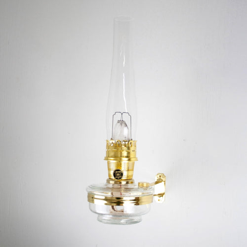 Handcrafted brass wall bracket with clear glass oil lamp and tall chimney, designed for classic Aladdin lamps, featured in Lamps & Lighting, Oil Lamps, Wall Lamps, Best Sellers, and Promo Eligible collections.