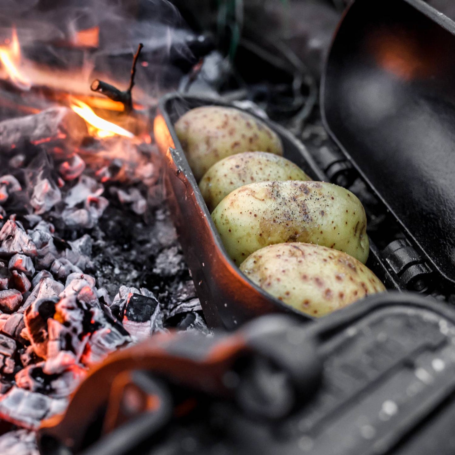Cast iron potato cooker roasting seasoned potatoes over glowing embers, ideal for Farm, Garden & Tool, Camping, Best Sellers, and Promo Eligible collections.