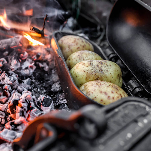 Cast iron potato cooker roasting seasoned potatoes over glowing embers, ideal for Farm, Garden & Tool, Camping, Best Sellers, and Promo Eligible collections.