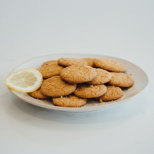 Plate of Amish made crispy lemon snap cookies with a golden texture and zesty citrus flavor, accompanied by a fresh lemon slice, ideal for Kitchen & Food, Snacks and Sweets, and Best Sellers collections.