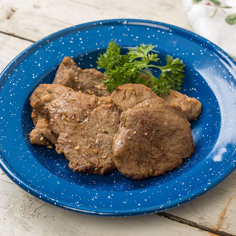Cooked freeze-dried sirloin steak slices served on a blue speckled enamel plate with a garnish of fresh parsley, highlighting a long-lasting, USA-made emergency food option.