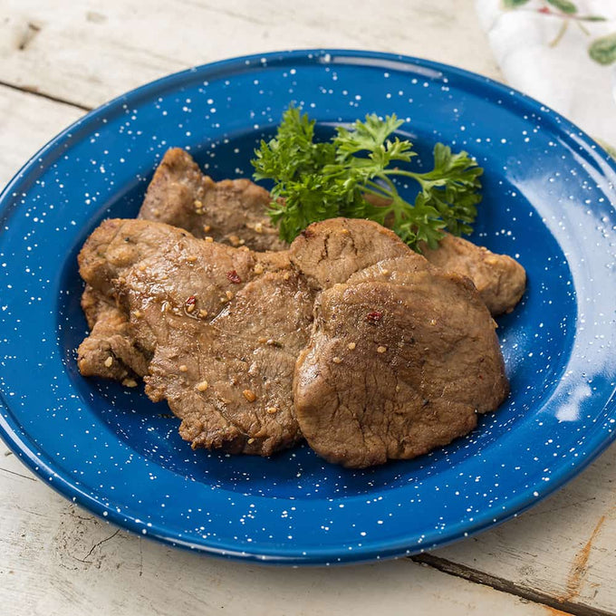 Cooked freeze-dried sirloin steak slices served on a blue speckled enamel plate with a garnish of fresh parsley, highlighting a long-lasting, USA-made emergency food option.
