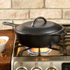Deep cast iron chicken fryer with lid featuring self-basting nubs, pre-seasoned and designed for even heating, shown on a gas stove in a kitchen setting.