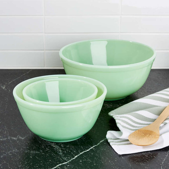 Set of three nested glass mixing bowls in soft green on a dark kitchen countertop with a wooden spoon and striped cloth, perfect for Kitchen & Food and Baking Supplies collections.
