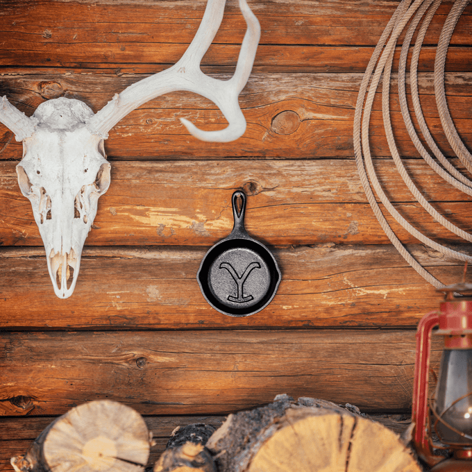 Handcrafted cast iron skillet featuring a distinct embossed Power Y design, displayed on a rustic wooden wall with a steer skull, rope, and lantern for Kitchen & Food, Cookware, Cast Iron, USA Made, and Best Sellers collections.