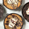 Four handcrafted, Amish-made cast iron skillets with fresh-baked desserts topped with ice cream and chocolate drizzle, featured in Kitchen & Food, Camp, and USA Made collections.