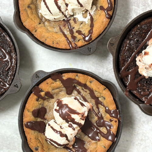 Four handcrafted, Amish-made cast iron skillets with fresh-baked desserts topped with ice cream and chocolate drizzle, featured in Kitchen & Food, Camp, and USA Made collections.