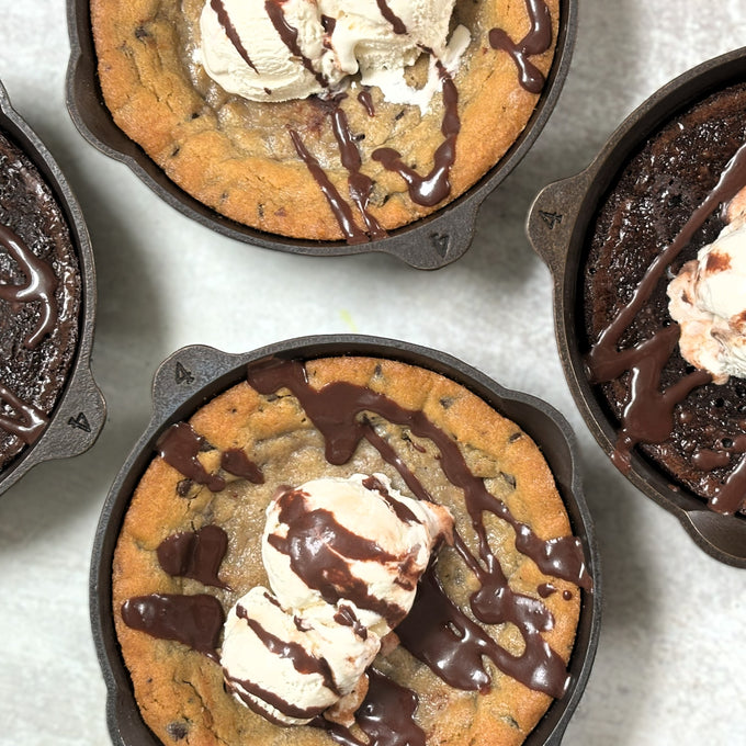 Four handcrafted, Amish-made cast iron skillets with fresh-baked desserts topped with ice cream and chocolate drizzle, featured in Kitchen & Food, Camp, and USA Made collections.