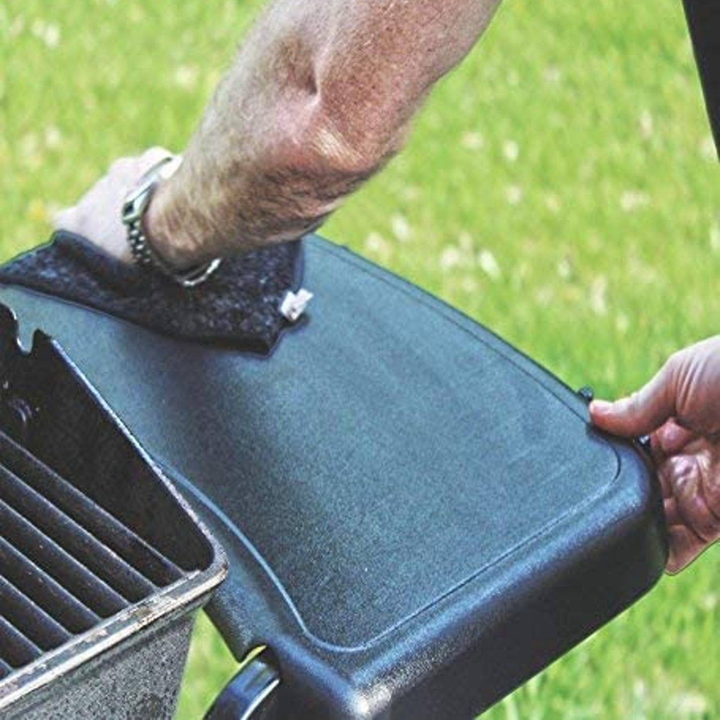 Person wiping a black BBQ grill side shelf outdoors with a cloth, demonstrating maintenance and cleaning in household and grilling collections.