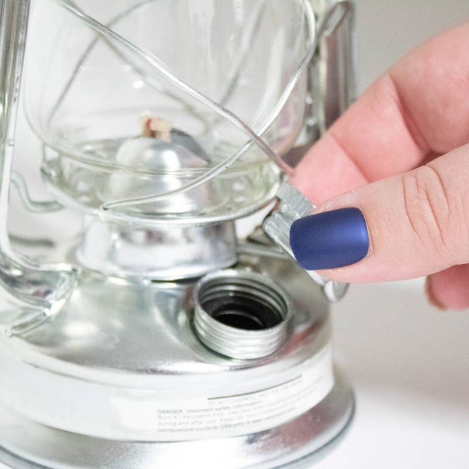 Close-up of a hand adjusting the glass globe on a compact galvanized metal lantern, showcasing durable weather-resistant construction suitable for camping, farm, and emergency lighting.