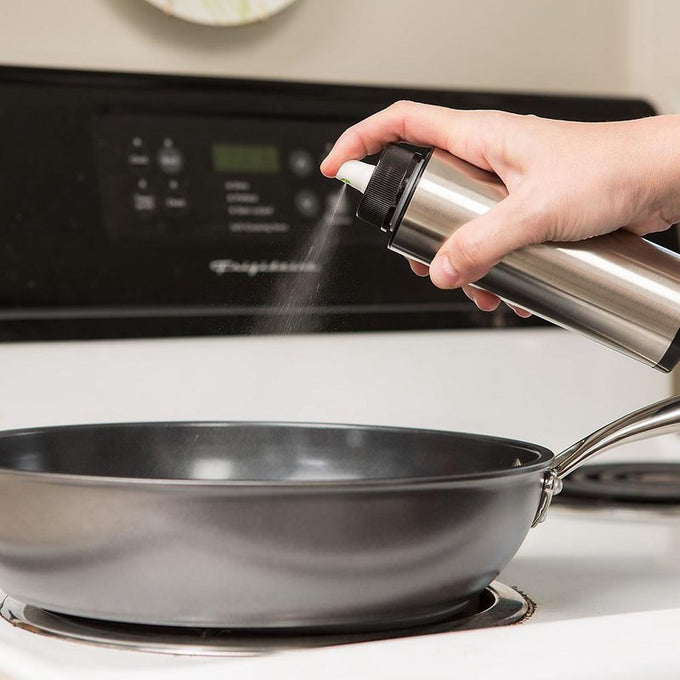 Handheld stainless steel oil mister spraying a fine mist over a nonstick frying pan on stovetop, perfect for Kitchen & Food, Cookware, Baking Supplies, and Kitchen Gadgets collections