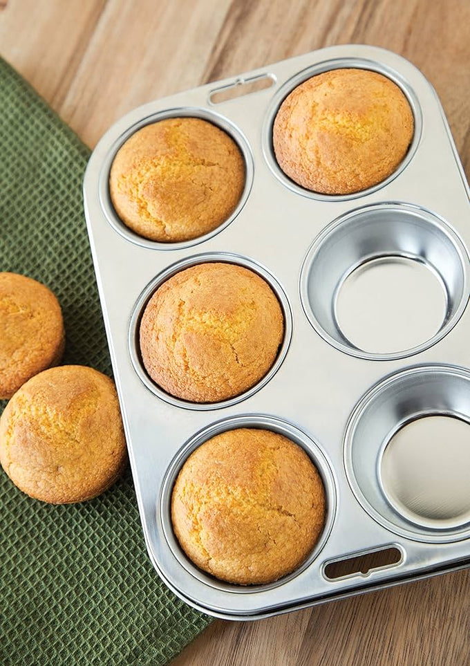 Stainless steel muffin pan with six cups holding freshly baked golden muffins, displayed on a wooden surface next to a green textured cloth, suitable for Kitchen & Food and Baking Supplies collections.