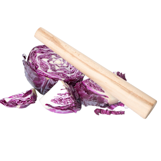 Smooth natural wood stomper resting on freshly cut purple cabbage wedges, designed for tamping down fermenting foods in kitchen, food preservation, and pickling tasks.