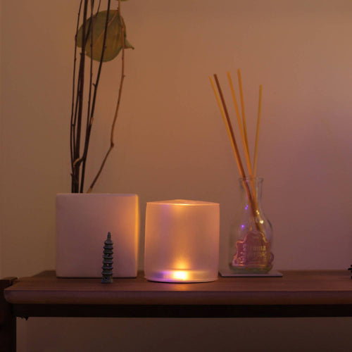 Soft glowing inflatable solar candle casting a warm flickering light beside decorative items on a wooden surface, ideal for cozy indoor or outdoor settings in camping and lighting collections.