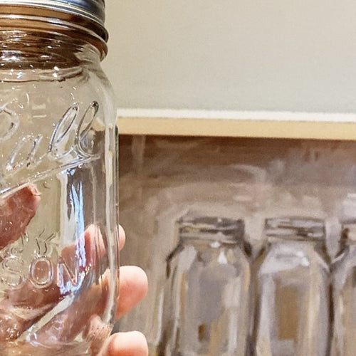 Clear glass regular-mouth canning jar with metal lid held in hand against a background of unscrewed similar jars, perfect for Kitchen & Food, Food Preservation, Canning, USA Made, Best Sellers, and Promo Eligible collections.