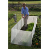 Man gardening with a sturdy micromesh pest and wind barrier enclosing a raised bed, protecting crops from pests while allowing sunlight and air in, set in a lush garden.