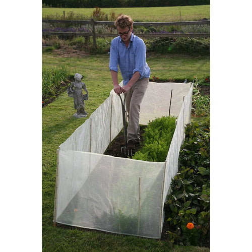 Man gardening with a sturdy micromesh pest and wind barrier enclosing a raised bed, protecting crops from pests while allowing sunlight and air in, set in a lush garden.