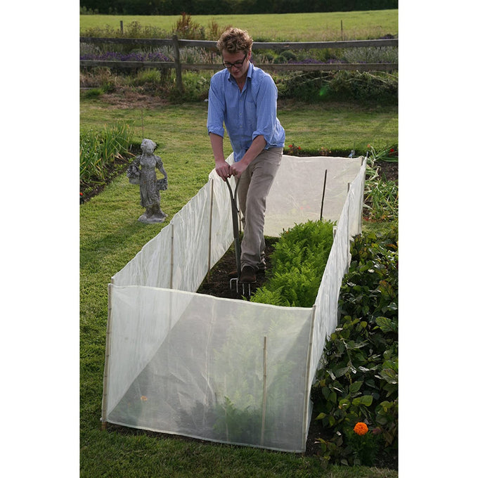 Man gardening with a sturdy micromesh pest and wind barrier enclosing a raised bed, protecting crops from pests while allowing sunlight and air in, set in a lush garden.