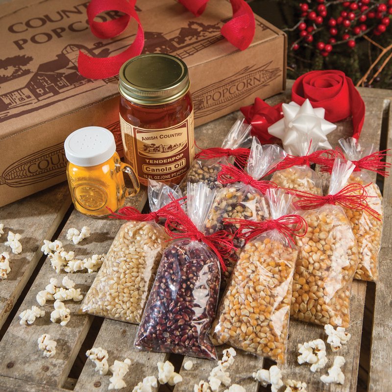 Collection of eight small bags filled with various popcorn kernels alongside a jar of Amish-made canola oil and a shaker, displayed with festive red ribbons on rustic wood, featured in Kitchen & Food, Snacks and Sweets, USA Made, Amish Made, and Best Sellers.