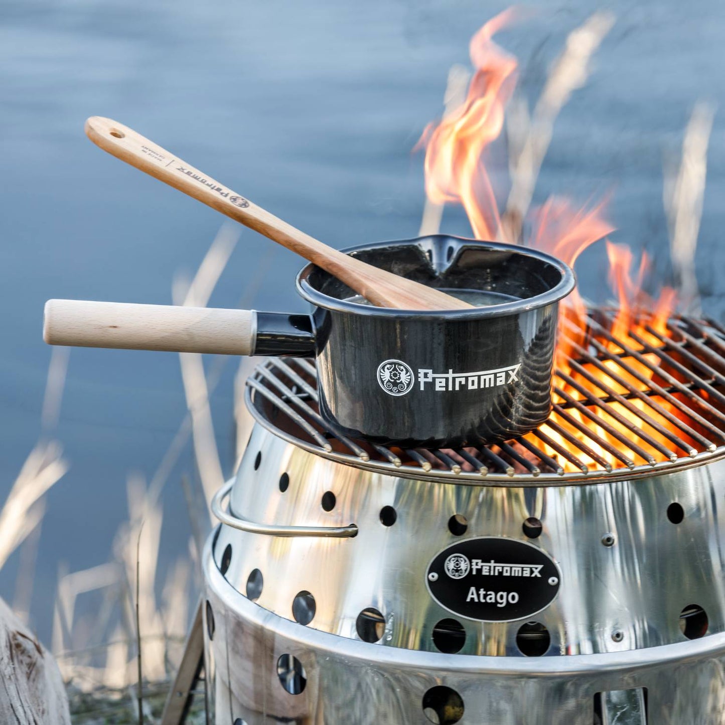 Durable black enamel pan with a wooden handle cooking over an open flame on a stainless steel grill, ideal for Camping, Kitchen & Food, Cookware, and outdoor use collections.