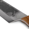 Close-up of a handcrafted chef's knife blade with a hammered textured finish and sharp edge, featuring a smooth walnut handle, ideal for outdoor cooking and food preparation collections.