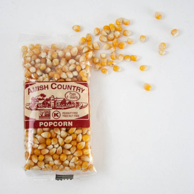 Clear bag of handcrafted Amish Country popcorn kernels with some kernels spilled onto a white surface, featured in Kitchen & Food, Snacks and Sweets, Popcorn, and USA Made collections.
