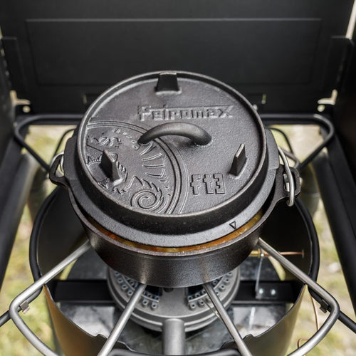Black cast iron Dutch oven with flat base and embossed lid featuring decorative motifs and sturdy handles, cooking on a portable gas stove, perfect for Kitchen & Food, Cookware, Cast Iron, Best Sellers, Promo Eligible collections.