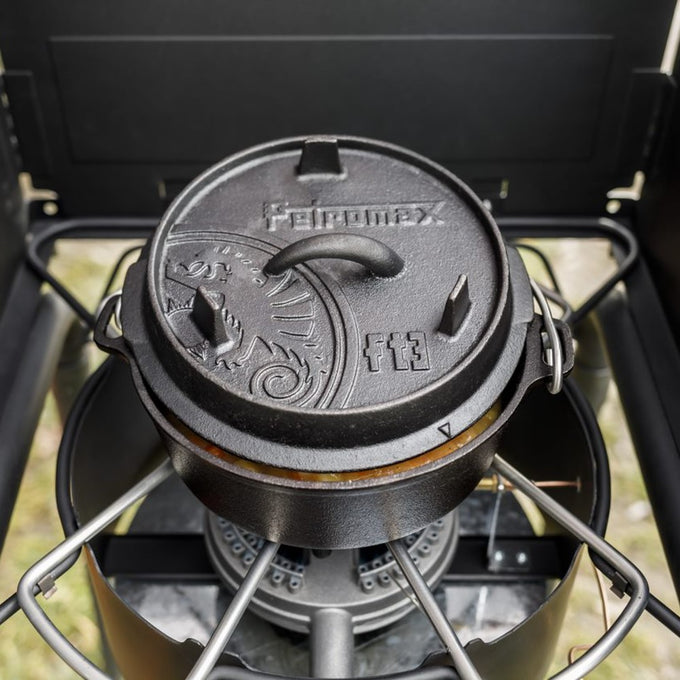 Black cast iron Dutch oven with flat base and embossed lid featuring decorative motifs and sturdy handles, cooking on a portable gas stove, perfect for Kitchen & Food, Cookware, Cast Iron, Best Sellers, Promo Eligible collections.