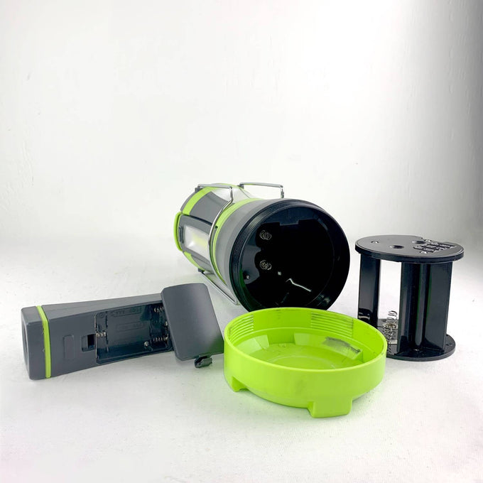 Disassembled LED camping lantern and detachable flashlight components in black and bright green, showcasing the battery compartment and internal parts for outdoor and emergency lighting use.