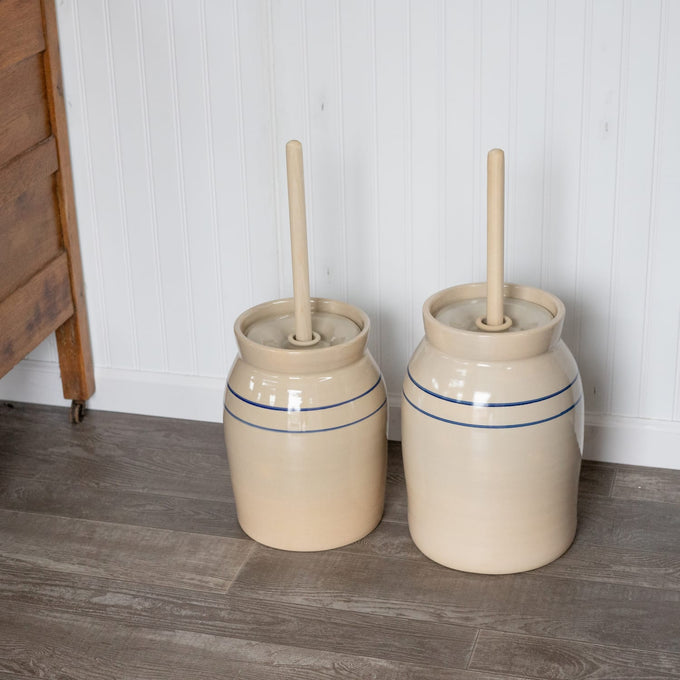 Two handcrafted stoneware butter churns in natural stone color with smooth unfinished wooden dashers and classic double blue stripes, made in USA, featured in Kitchen & Food, Specialty Equipment, Making Butter, USA Made, Best Sellers, and Promo Eligible collections.