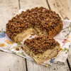 Close-up of a freshly baked pecan roll slice topped with chopped pecans and caramel glaze, handcrafted and made in USA, presented on a floral cloth in a rustic kitchen setting.