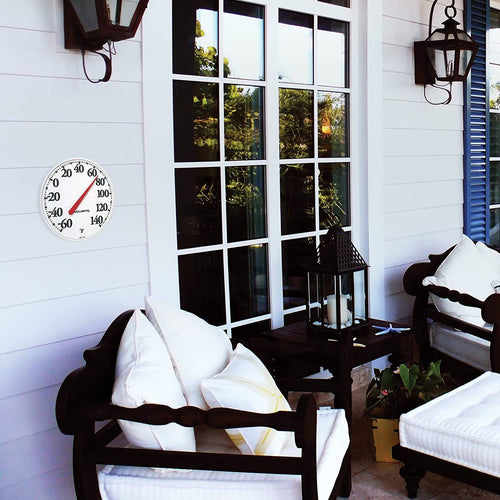 White 12-inch diameter indoor outdoor thermometer with large black numbers and red needle, mounted on light siding near dark wood patio furniture with white cushions, featured in Farm, Garden & Tool and Garden Accessories collections.