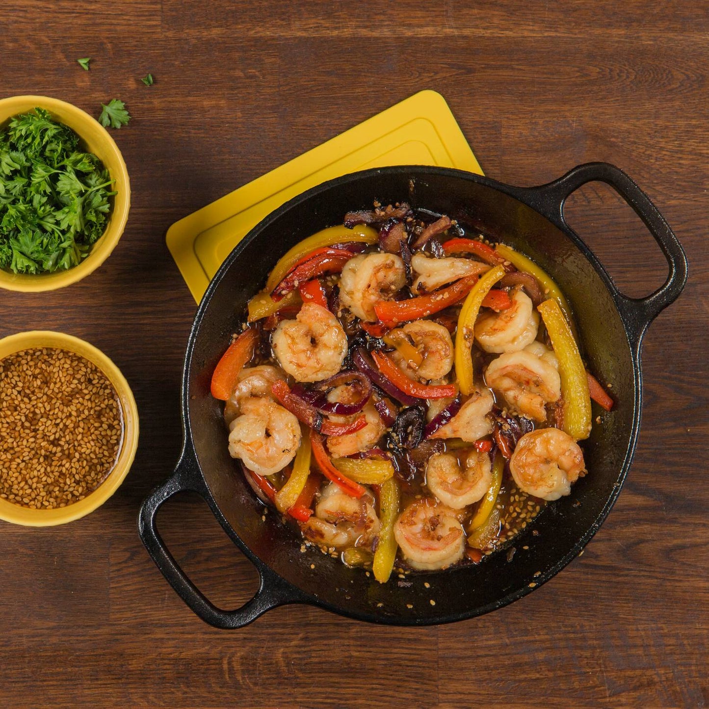 Round cast iron pan filled with sautéed shrimp and colorful bell peppers, accompanied by bowls of fresh herbs and mustard seeds, ideal for Kitchen & Food, Cookware, Cast Iron, Best Sellers, Promo Eligible collections.