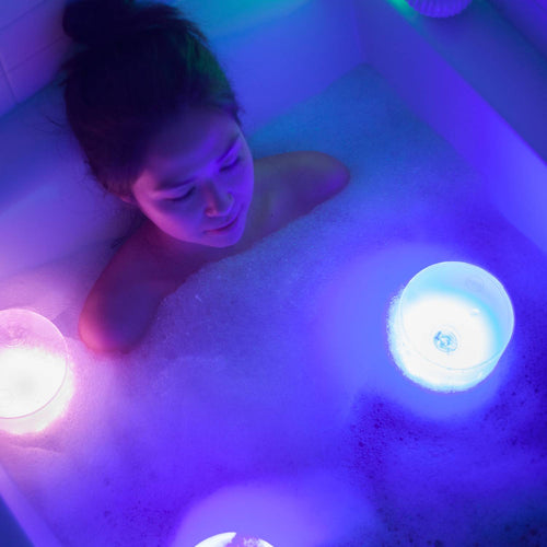Person relaxing in a bubble bath illuminated by soft, colorful glowing inflatable solar LED lights, creating a serene atmosphere for home relaxation and lighting.