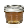 Clear regular-mouth glass jelly jar with quilted texture and silver metal lid, filled with honey-colored preserve, ideal for food preservation and canning, made in USA.