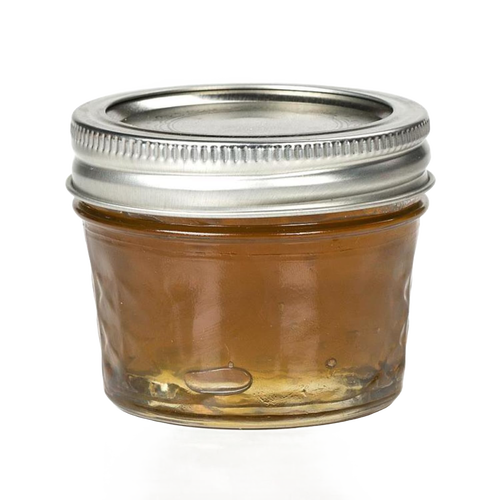 Clear regular-mouth glass jelly jar with quilted texture and silver metal lid, filled with honey-colored preserve, ideal for food preservation and canning, made in USA.