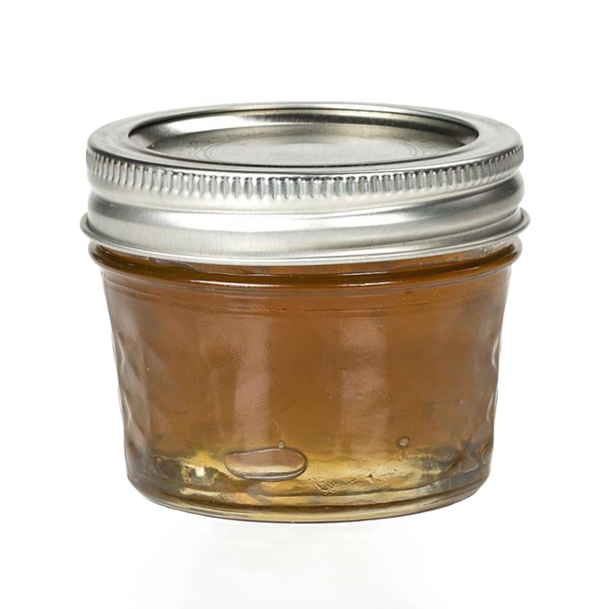 Clear regular-mouth glass jelly jar with quilted texture and silver metal lid, filled with honey-colored preserve, ideal for food preservation and canning, made in USA.