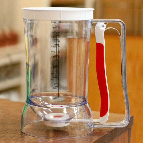 Clear plastic batter dispenser with ergonomic white and red soft-grip handle, featuring measurement markings for precise pouring, ideal for Kitchen & Food, Baking Helpers, and Promo Eligible collections.