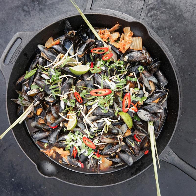 Cast iron skillet with long handle filled with cooked mussels, garnished with sliced red chili, lime wedges, bean sprouts, and herbs, ideal for Farm, Garden & Tool, Kitchen & Food, Camping, Cookware, Cast Iron, Best Sellers, Promo Eligible collections.