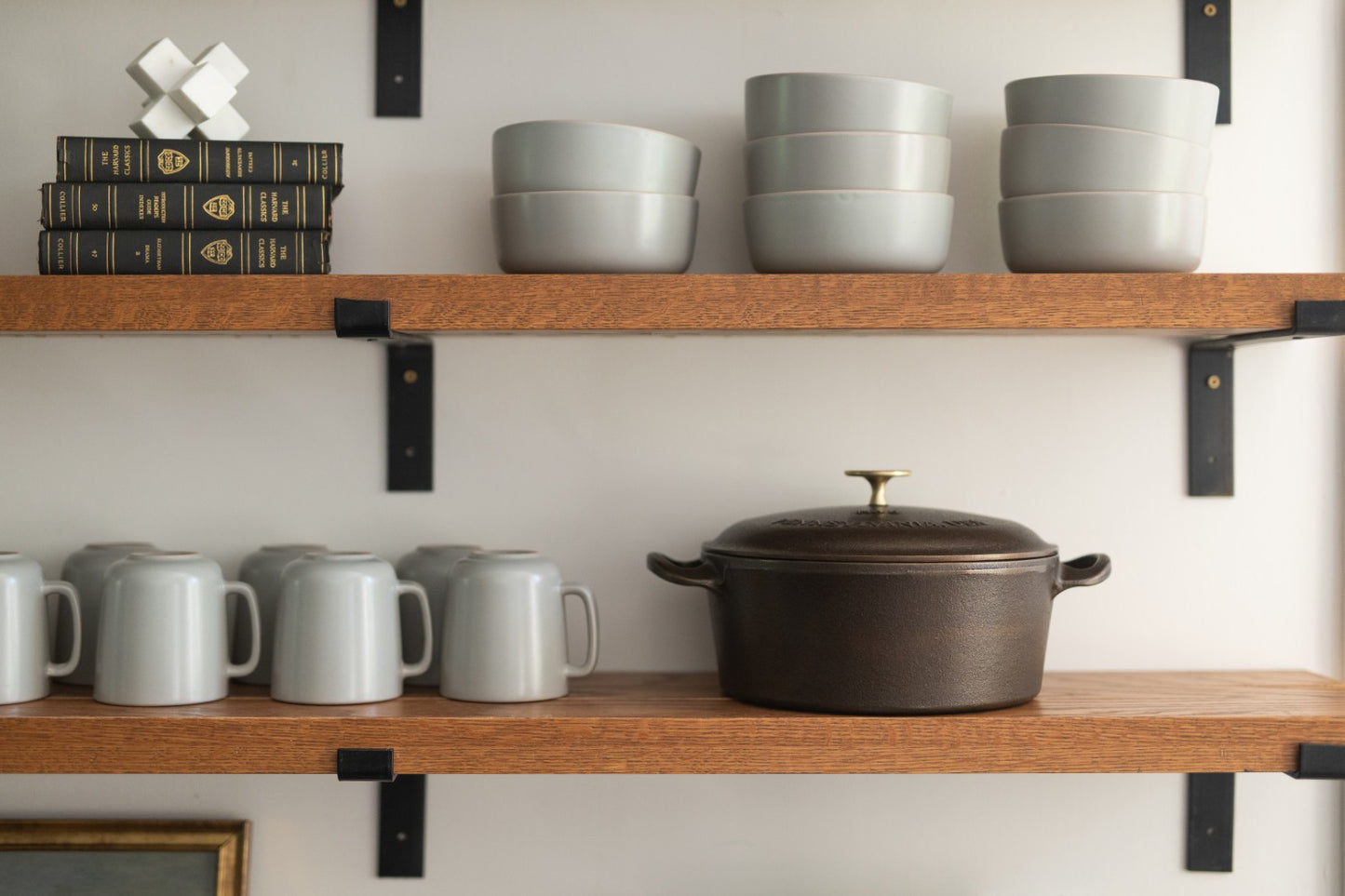 Handcrafted, Amish-made cast iron Dutch oven with a dark finish, displayed alongside gray ceramic mugs and bowls on rustic wooden shelves, fitting Farm, Kitchen & Food, and USA Made collections.