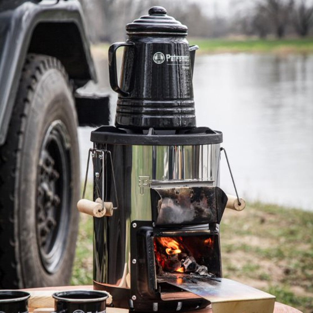 Black enameled steel percolator on a portable wood-burning stove near a riverside, ideal for brewing aromatic coffee or tea, featured in Farm, Garden & Tool, Camping, Kitchen & Food, and Brewing Coffee and Tea collections.