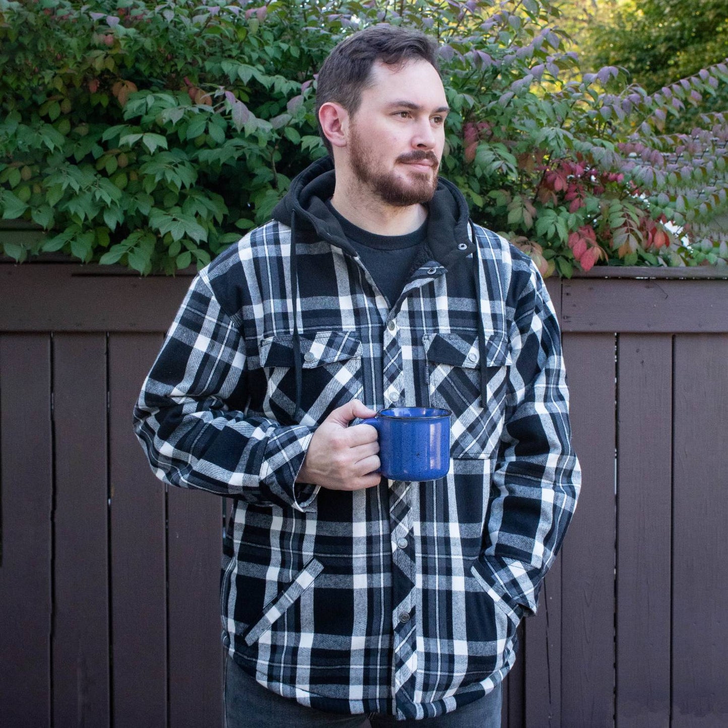 Man wearing a handcrafted oversize black and white plaid flannel jacket with a hooded sherpa lining, holding a blue enamel mug, featured in Health & Wellness and Clothing collections.