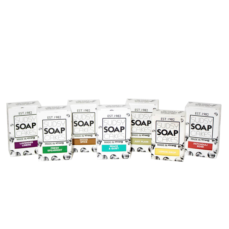 Row of handcrafted Sudsy Soapcakes bars in assorted natural scents including lavender, spearmint, wood spice, patchouli rose, lemon drop, and peace & quiet, made in USA, featured in Health & Wellness and Soaps collections.