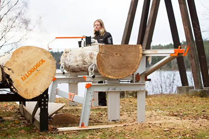 Portable chain sawmill with sturdy metal frame and orange accents, supporting large logs outdoors near a lake, featured in Farm, Garden & Tool, Wood Cutting and Hauling, and Best Sellers collections.