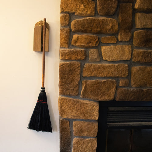 Handcrafted Amish made wooden wall broom holder in natural finish mounted beside a stone fireplace wall, designed for organized broom storage in Home & Decor and Household Helpers collections.