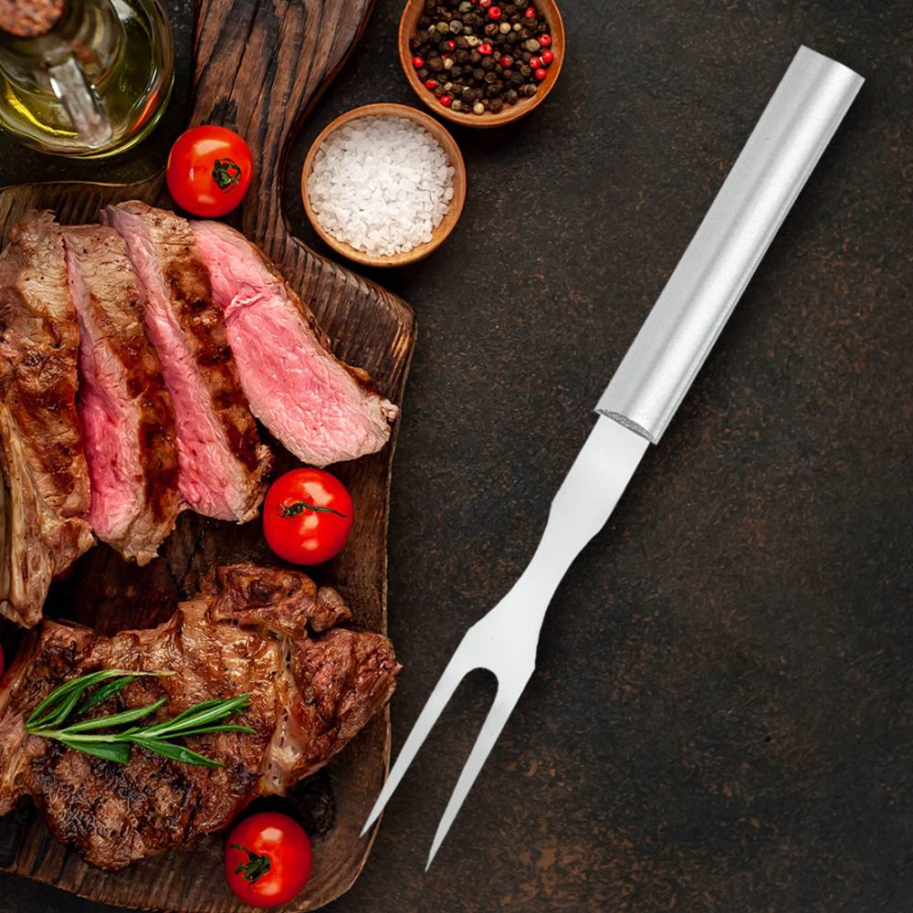 Carving fork with long stainless steel tines and smooth metal handle resting beside sliced grilled steak garnished with cherry tomatoes, rosemary, salt, and pepper, ideal for Kitchen & Food, Storage and Serving, USA Made, Best Sellers, and Promo Eligible collections.