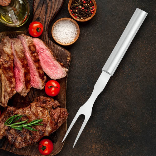 Carving fork with long stainless steel tines and smooth metal handle resting beside sliced grilled steak garnished with cherry tomatoes, rosemary, salt, and pepper, ideal for Kitchen & Food, Storage and Serving, USA Made, Best Sellers, and Promo Eligible collections.