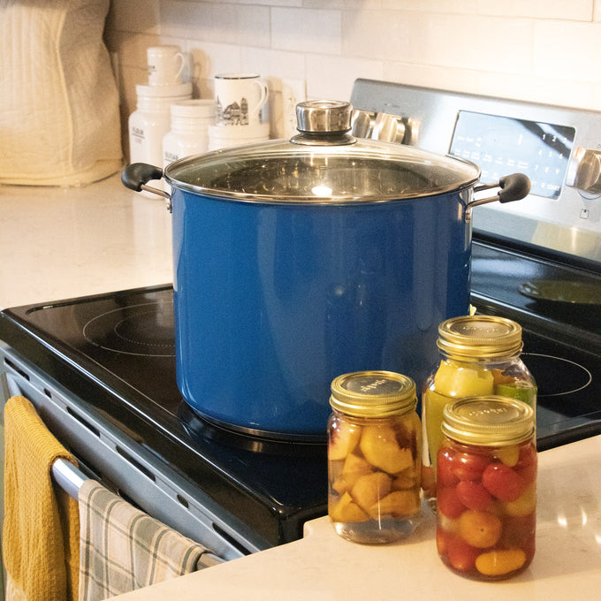 Blue water bath canner with glass lid and black handles on stovetop next to three sealed jars of preserved fruits, featured in Kitchen & Food, Food Preservation, and Canning collections.