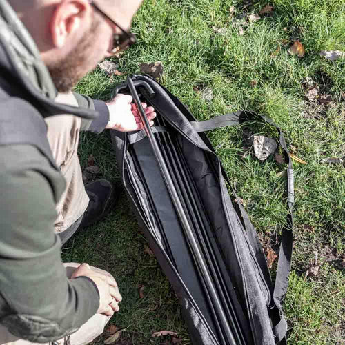 Man placing metal fire bridge poles into a black ripstop transport bag with shoulder strap, designed for durable and water-repellent storage, ideal for camping and outdoor use.