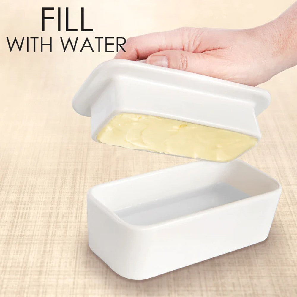 Hand holding the ceramic lid with butter over the rectangular base filled with water, demonstrating the French butter crock method for airtight butter storage in Kitchen & Food and Specialty Equipment collections.